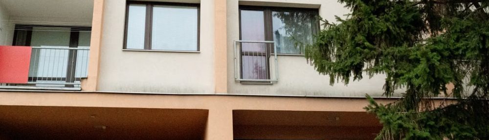 Three women waving to an elderly woman on an apartment balcony in Prague.