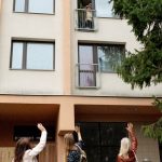 Three women waving to an elderly woman on an apartment balcony in Prague.