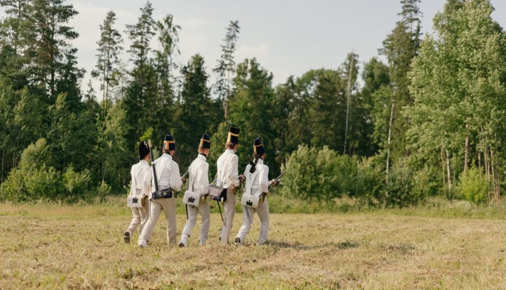 Group of soldiers in historical uniforms marching through a forest clearing.