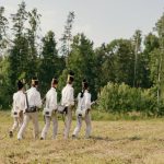 Group of soldiers in historical uniforms marching through a forest clearing.
