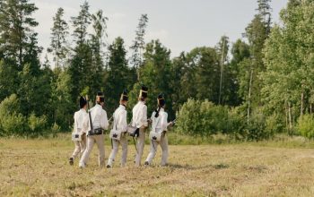 Group of soldiers in historical uniforms marching through a forest clearing.