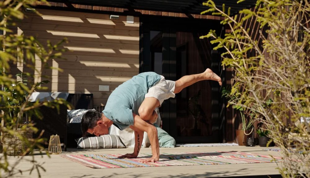 Man practicing yoga handstand balance pose on a sunny outdoor veranda.