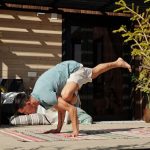 Man practicing yoga handstand balance pose on a sunny outdoor veranda.