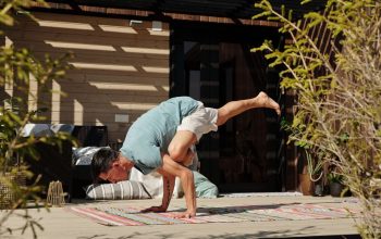 Man practicing yoga handstand balance pose on a sunny outdoor veranda.